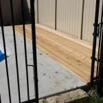 new wooden deck constructed by stittsville deck builder next to a metal fence with a blue tarp in the background on a sunny day.