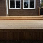 a newly constructed wooden deck with railings, crafted by stittsville deck builder, adjacent to a residential building.