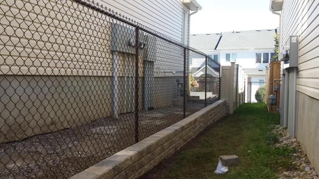 chain-link fence benefits include separating residential properties with a walkway and landscaped area featuring gravel and retaining wall blocks, fence styles