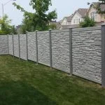 a simtek stone-textured privacy fence borders a manicured lawn in a residential neighborhood.