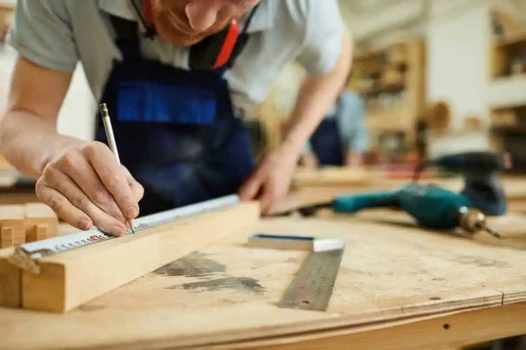 a person in a workshop measuring and marking wood with a ruler and pencil, with tools scattered around on the workbench, dog fence installation, fence builder