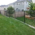 a residential backyard, benefiting from a chain-link fence and well-maintained lawn, is adjacent to a two-story house.