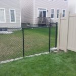 A residential backyard benefitting from a chain-link fence adjoining a beige vinyl privacy fence, with houses featuring decks in the background.