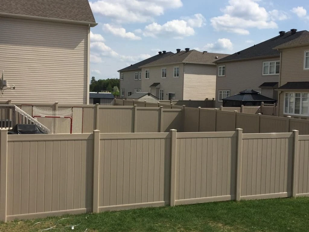 backyard with a tall beige privacy fence, installed by ottawa experts, surrounded by suburban houses under a partly cloudy sky.