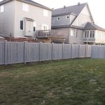 A residential backyard with a benefits of using a SimTek fence, houses visible in the background, and a yellow garden hose lying on the grass.