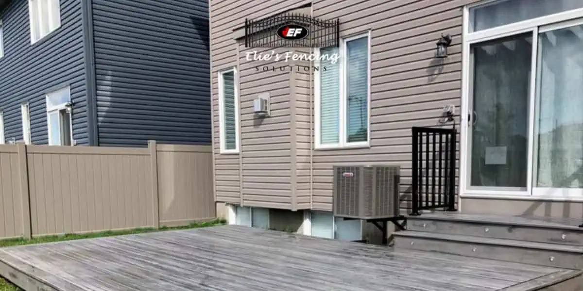 A residential backyard featuring a wooden deck and beige vinyl fencing with the logo "ef elite fencing solutions" superimposed at the top center.