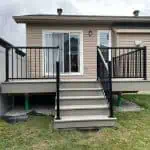 a small wooden custom deck with black railings and a stairway leading to the backyard of a tan siding house, deck design