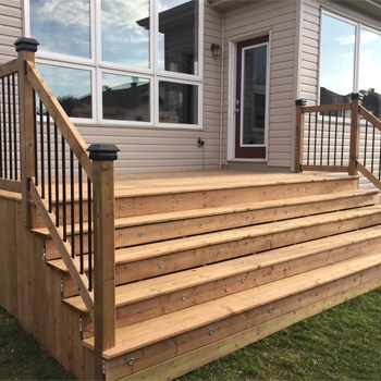 Custom wooden deck with stairs leading to a house door, featuring railings and a green lawn surrounding the structure.