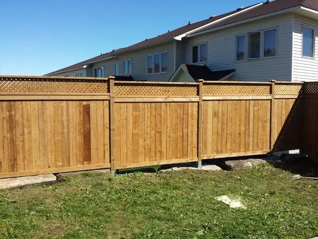 a newly constructed wooden fence stands in a backyard on a sunny day, with residential houses visible in the background.