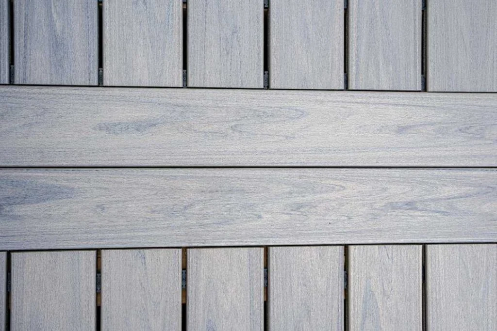 close-up of a gray wooden deck surface with visible grain patterns, reminiscent of interlock paving designs often seen in ottawa. the boards are arranged in parallel lines, with a larger central plank flanked by smaller ones.