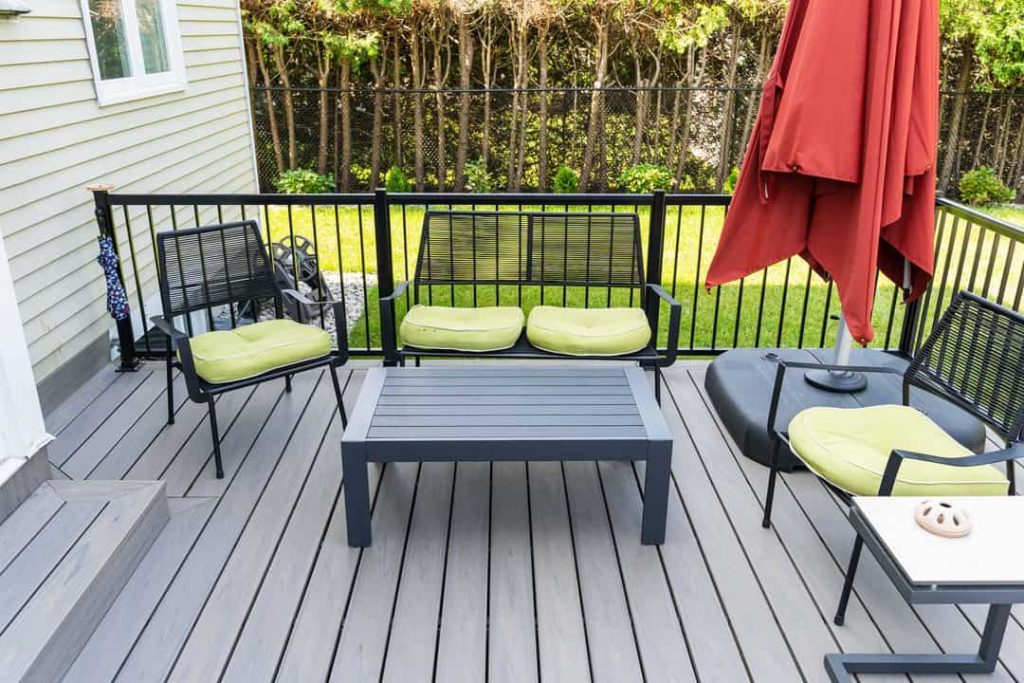 A well-maintained outdoor patio area with black furniture and green cushions, accompanied by a red umbrella closed to the side.