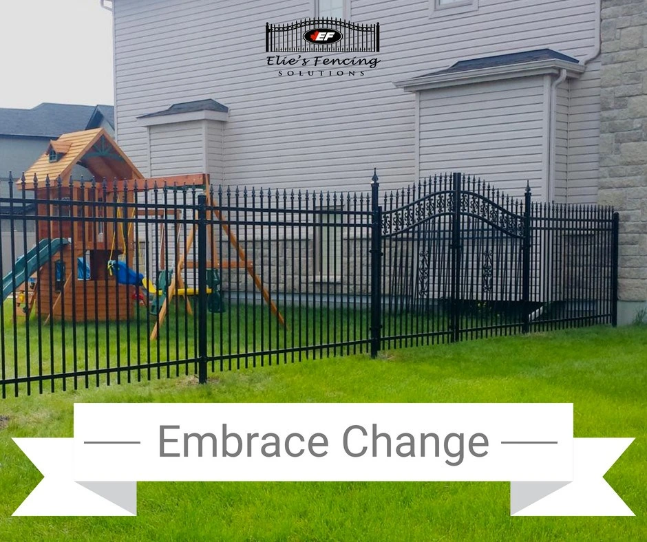 black metal fence surrounding a backyard with grass, a wooden playset, and a house in the background, labeled "embrace change" by elie's fencing solutions.