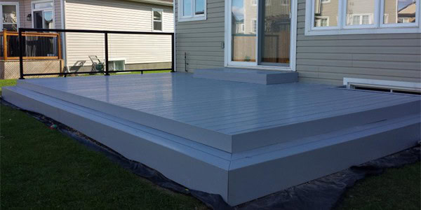 Low-profile, gray PVC decking in a backyard with a railing and neighboring houses in the background.