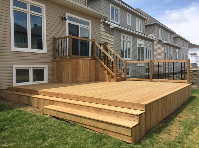 newly constructed wood deck with railing and stairs attached to a suburban home, surrounded by a grassy yard.