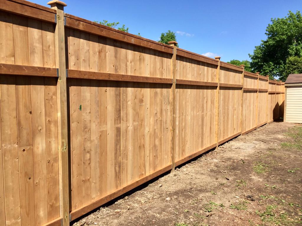 A new long wooden privacy fence with vertical planks under clear blue sky, separating residential backyards.
