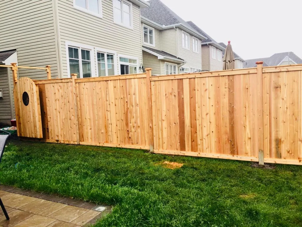 a new wooden privacy fence with a circular cut-out design stands in a backyard, adjacent to a two-story house and green lawn.