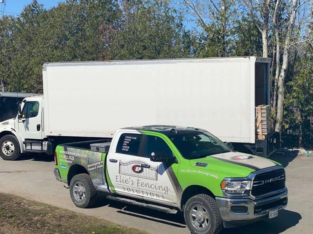 a green and white branded pickup truck from ellie's temporary fencing solutions parked in front of a large white semi-truck under a clear blue sky.