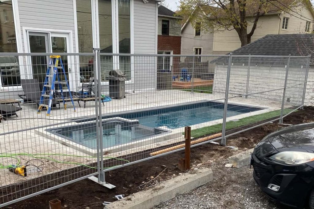 A residential backyard under construction, featuring a new pool and spa enclosed by temporary fences, with construction equipment and materials scattered around. temporary fences for construction