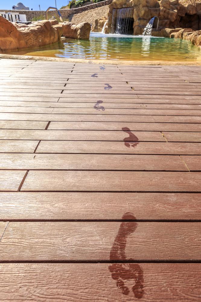 Wet footprints on a wooden boardwalk, constructed using durable fencing materials, leading towards a pool with a small waterfall in the background, Carports and pergolas