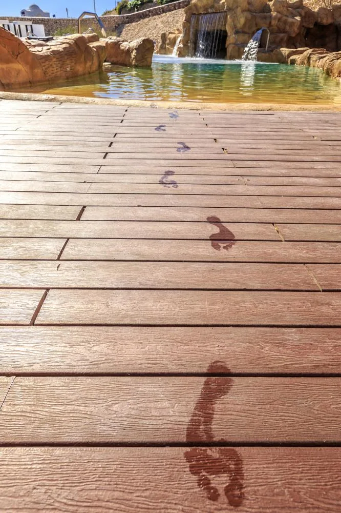 Wet footprints on a wooden boardwalk, constructed using durable fencing materials, leading towards a pool with a small waterfall in the background, Carports and pergolas