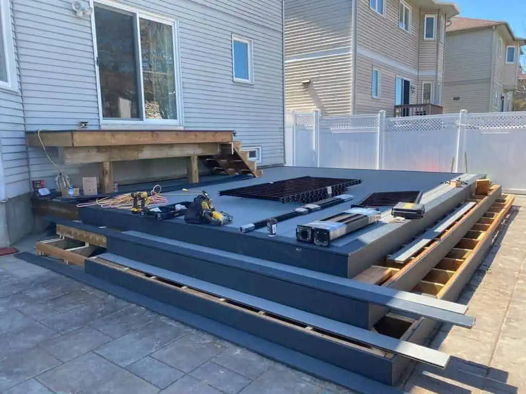 backyard with partially constructed deck featuring wooden framework and various tools and materials laid out, preparing for the installation of composite decking.