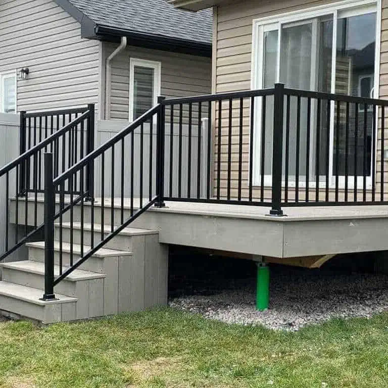 a gray composite decking with a black metal railing, connected to a house with beige siding. the deck features a set of stairs leading to a grassy area below.