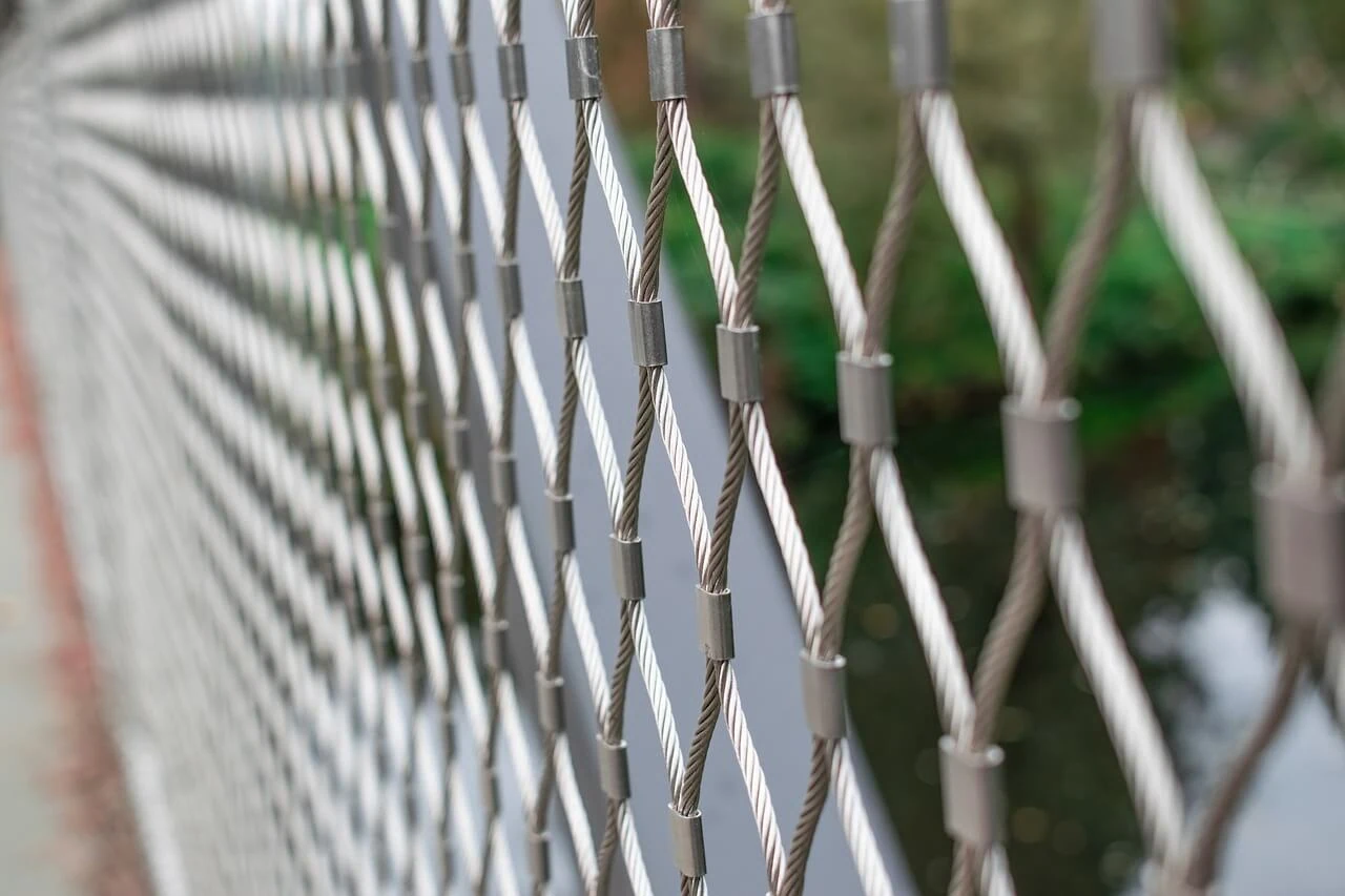 close-up of a wire mesh fence with greenery blurred in the background. the perspective, artfully designed by a skilled fence contractor, shows the fence receding into the distance.