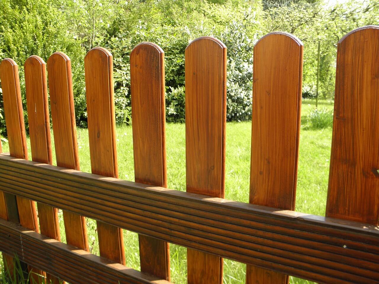 A close-up of a wooden picket fence with vertical planks, crafted meticulously by a skilled fence contractor, with lush greenery in the background.