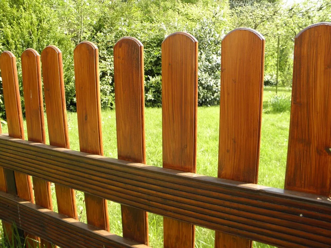 a close-up of a wooden picket fence with vertical planks, crafted meticulously by a skilled fence contractor, with lush greenery in the background.