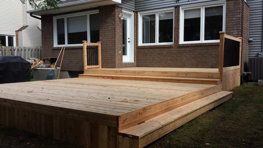 a custom deck with stairs leads to a house featuring a brick exterior and large windows.